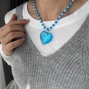 Close-up of a blue heart pendant necklace with blue and white beads on a person