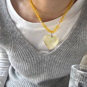 Detail of a bright yellow beaded necklace with a large translucent heart pendant on model
