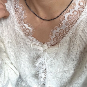 Gedetailleerd beeld van verfijnde zwarte kralenketting op witte kant gebreide top