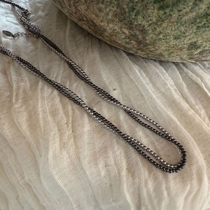 Detailweergave van dubbellaagse roestvrijstalen kralenketting op witte stof met steen