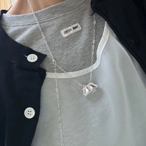 Collar largo con colgante de bolso plateado pulido sobre cárdigan negro para mujer