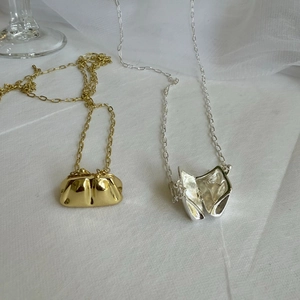 Detalle de mini colgantes de bolso en oro y plata sobre un fondo blanco con textura