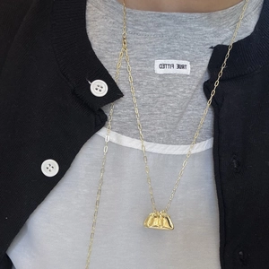 Detalle de un collar dorado con colgante de bolso plisado sobre una camiseta gris