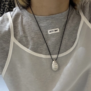 Detail view of a silver shell-shaped pendant on a minimalist black cord necklace