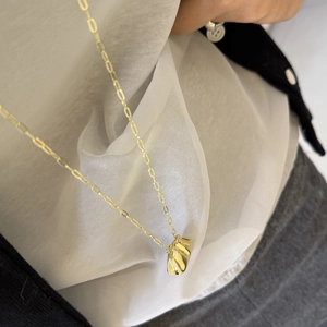 Detalle de collar dorado con colgante de textura de metal líquido y cadena minimalista