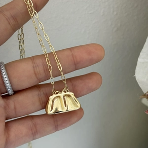 Primer plano de un collar con colgante de mini bolso dorado y cadena de eslabones ovalados