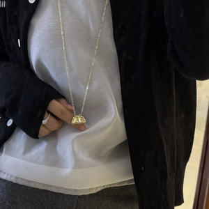 Primer plano del collar con colgante de bolso dorado sobre cárdigan negro elegante