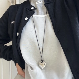 Close-up of a silver heart pendant necklace on a black cord worn by a model