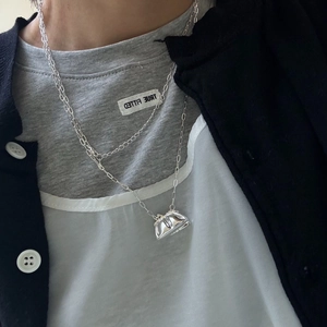 Detalle de un collar plateado con un colgante creativo en forma de bolso pulido brillante