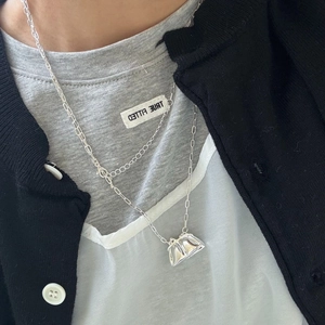Detalle de un collar de plata de doble capa con colgante de mini bolso y cadenas superpuestas