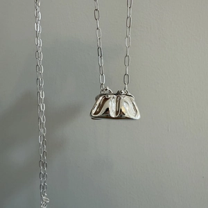 Detalle del colgante de mini bolso plateado en una cadena larga de eslabones ovalados