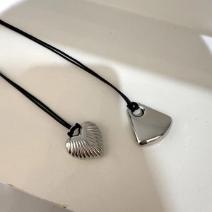 Macro shot of silver heart and trapezoid pendants with vertical shell texture on black cord