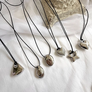 Detail shot of silver heart and geometric pendants with black cord on textured stone