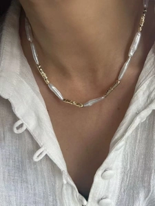 Detailed view of baroque pearl necklace with textured gold tubes on a linen shirt