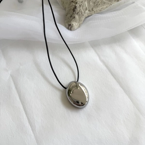 Macro shot of polished silver pebble heart pendant on a thin black cord necklace