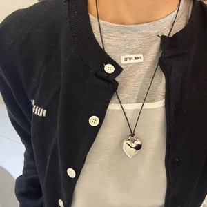 Close-up of a long silver heart pendant necklace on a minimalist black cord