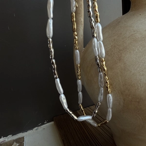 Artistic detail of baroque pearl necklace with fluid metallic beads on ceramic vessel