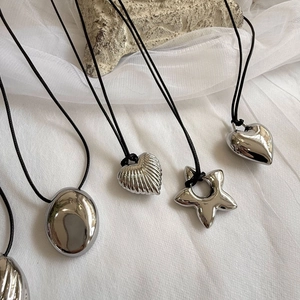 Close-up of silver heart and oval pendants on black cords over a textured grey rock