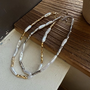 Detailed view of gold and silver baroque pearl necklaces on a textured wooden block
