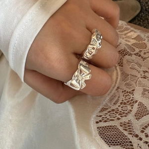 Close-up of silver textured bow and irregular rings worn with white lace background
