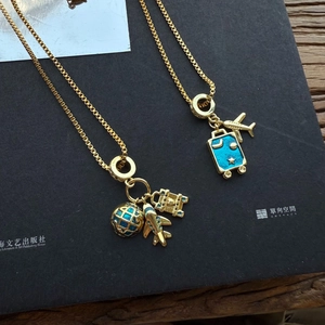 Detail van de gouden schakelketting met vliegtuig-, globe- en blauwe emaille kofferhangers