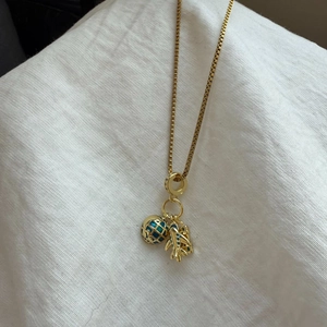 Detail van de gouden boxketting met hanger van een wereldbol en vliegtuig op linnen