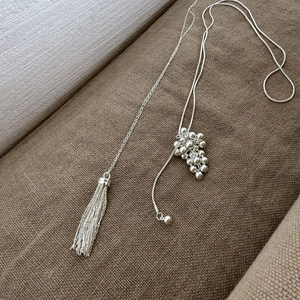 Detailed macro view of silver grape-shaped bead pendant and metallic tassel sweater chain