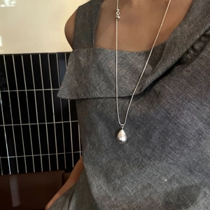 Minimalist silver water drop pendant necklace on model with grey linen top