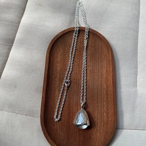 Macro detail of silver acorn pendant with fine textures and lobster clasp chain