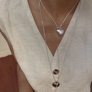 Detailed view of layered silver necklace set with heart and ring charms on linen fabric