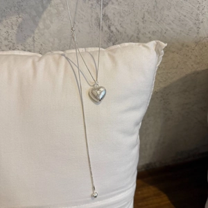 Macro view of textured silver heart pendant on a long adjustable tassel sweater necklace