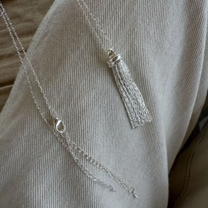 Close-up of a silver long tassel pendant necklace with lobster clasp on fabric background