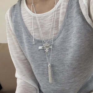 Close-up of a silver grape cluster necklace and tassel pendant on a layered chain style