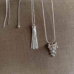 Detailed view of silver-plated grape cluster necklace and tassel pendant on brown fabric