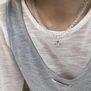 Detail van een transparante kralenketting met een zilveren metalen bloemenhanger op de borst