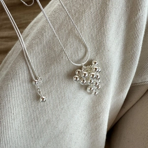 Detailed macro view of silver grape cluster pendant necklace on beige fabric texture