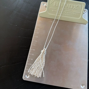 Detailed close-up of a silver tassel pendant necklace on a metallic measuring board