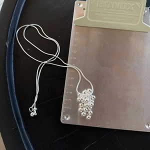 Macro detail of silver grape cluster pendant with snake chain and measurement scale