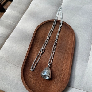 Detail of silver bell pendant with vertical textures on a fine link chain and lobster clasp
