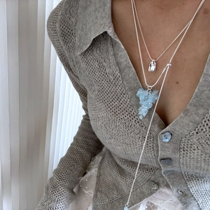 Detail of layered silver necklaces with a blue crystal grape pendant and square tag charm