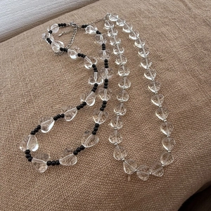 Detail van kralenketting met transparante hartkristallen en zwarte kralen op linnen