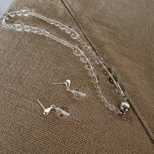 Platliggende set van transparante kristallen kralenketting en oorbellen op stof