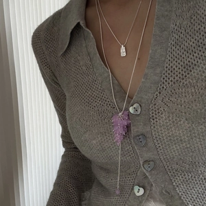 Detail of layered silver necklaces with purple grape-shaped bead pendant on grey cardigan