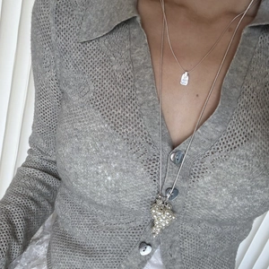 Close-up of grey openwork cardigan with heart buttons and pearl cluster necklace layering