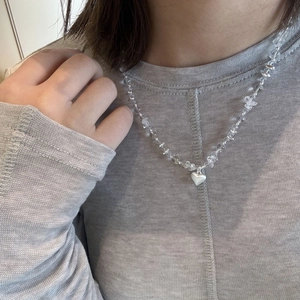 Ketting van onregelmatige kristallen kralen met witte hart hanger op grijze trui