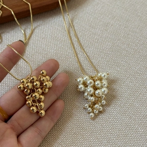 Close-up of elegant gold metal beads and pearl grape cluster pendants on snake chains