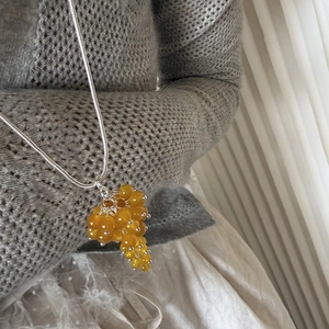Detail of yellow crystal grape pendant with silver snake chain on knitted sweater