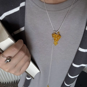 Close-up of a silver long chain necklace with yellow grape cluster pendant on model