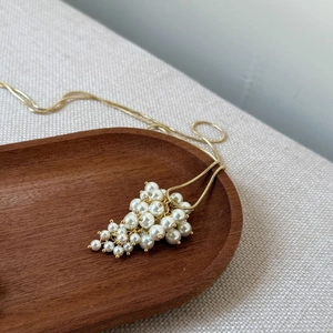 Detail of beaded grape cluster pendant on golden snake chain over wooden tray