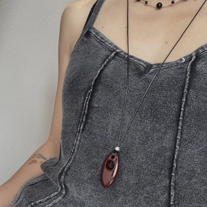 Detail of a deep reddish-brown oval pendant on a black woven long cord necklace